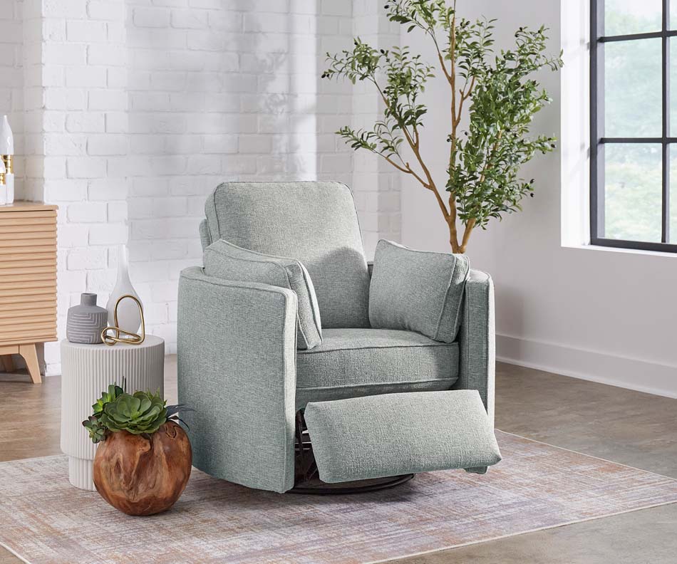 A photo of a dusty blue armchair with two arm cushions displays its footrest abilities in a white living room.