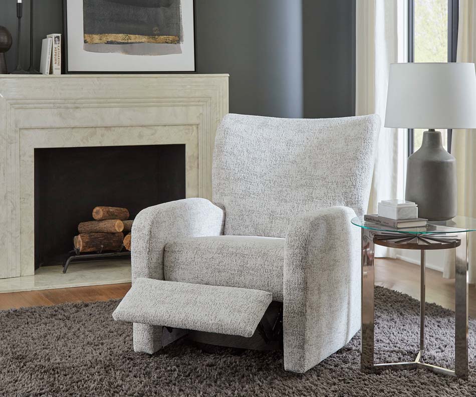 A photo of a modern styled grey armchair displays its footrest ability in front of a white fireplace.