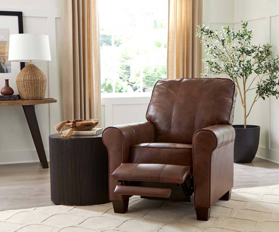 A photo of a brown leather armchair displays its footrest abilities next to a dark brown round side table.