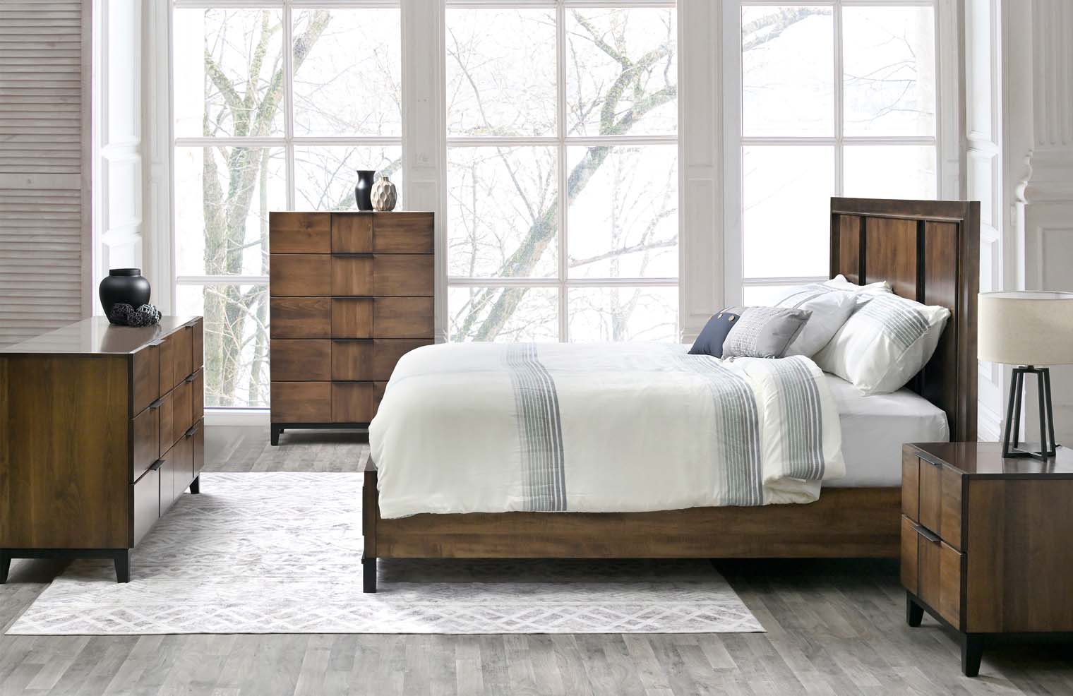 A bed sits on a shiny, dark wooden frame surrounded by a matching dresser, side table, and chest of drawers. They have a carved wooden inlay in the middle for decoration.