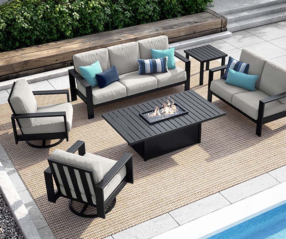 A display of cushioned outdoor patio furniture with a fire table sits by the poolside