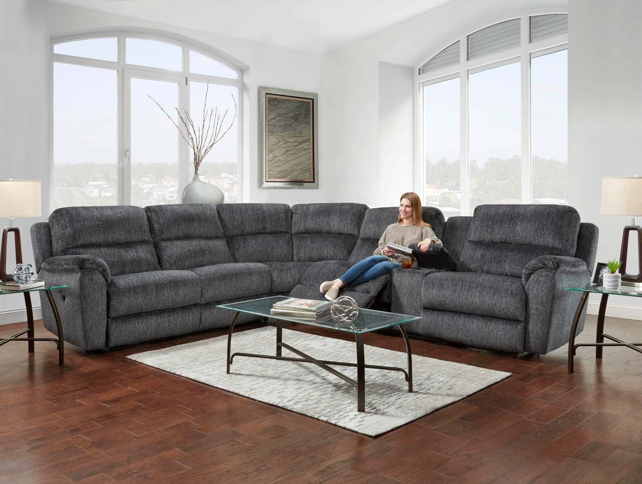 homestretch_contemporary_livingroom_adjustable-grey-sectional A woman sitting on a dark grey cushioned sectional displays the footrest capabilities.