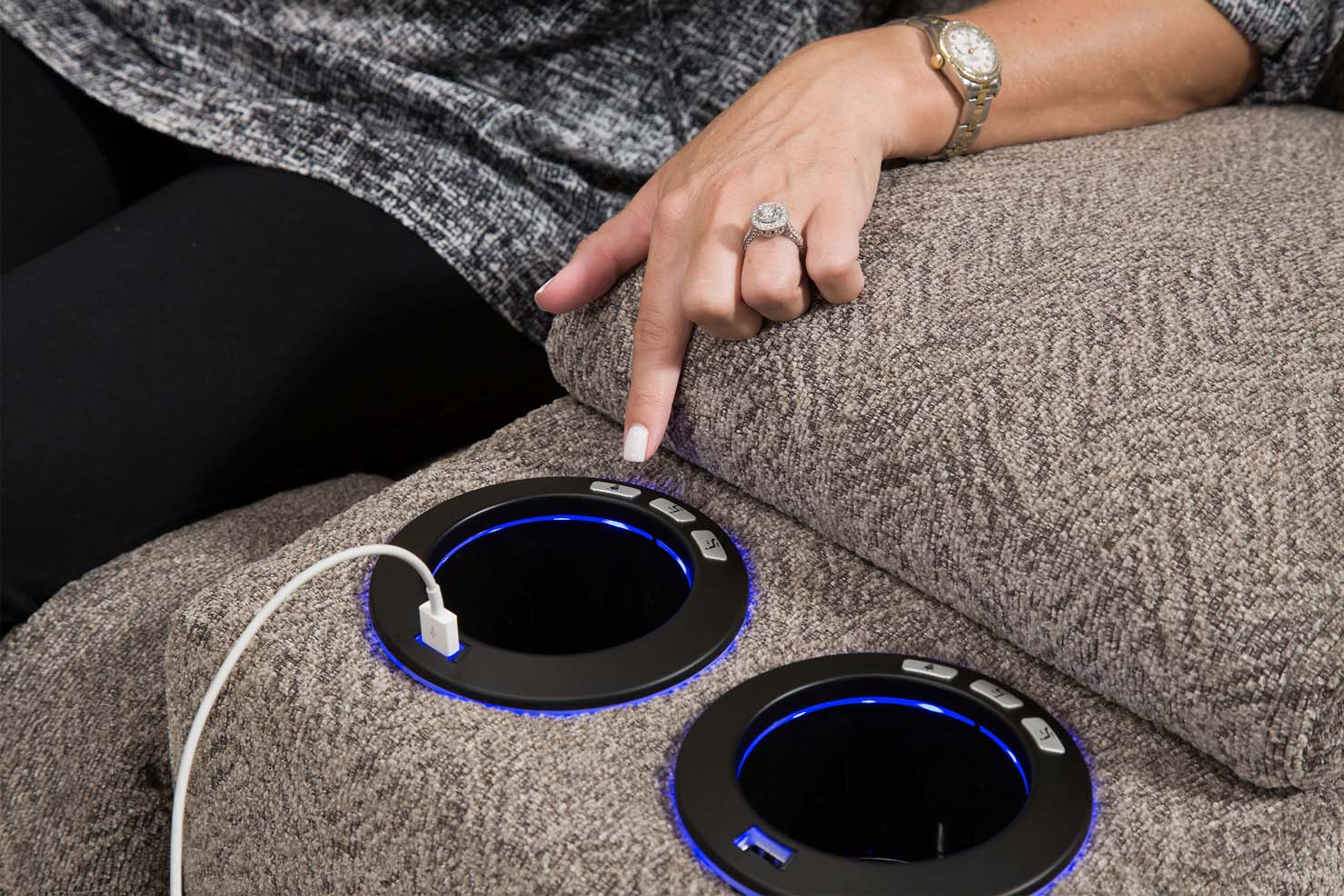A person’s hand points to a lit-up cup holder with a USB cable plugged in the outer rim.