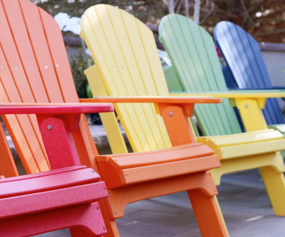 A photo of four Adirondack chairs in a row display some colors that they are available in (Red, yellow, green, and blue).