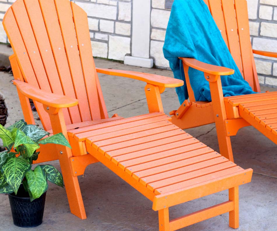 A photo of two bright orange, outdoor chaise lounges displays them sitting by a white brick wall.