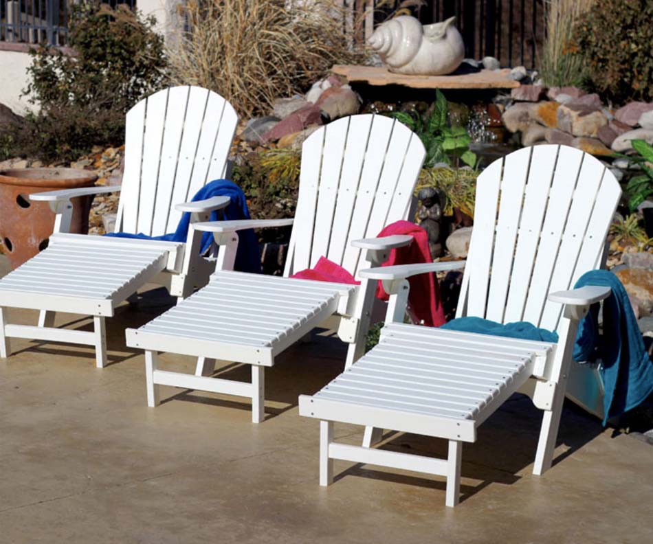 A photo of three bright white, outdoor chaise lounges with colorful towels draped across them.