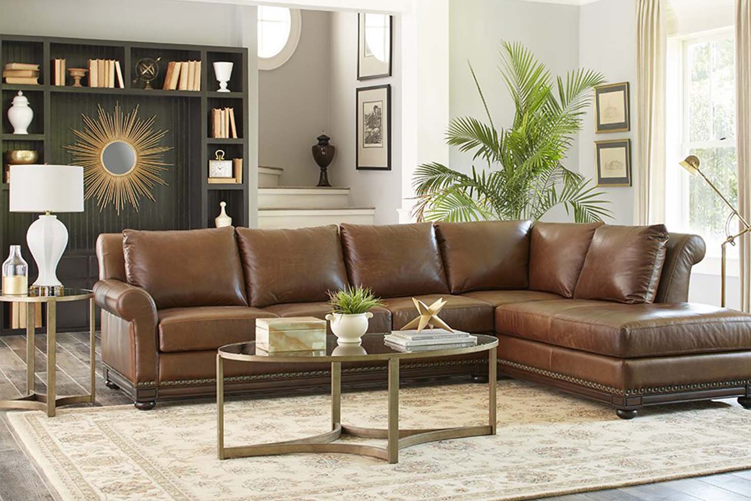 A shiny brown leather sectional with a carved wooden accent around the bottom sits in a modern style living room.