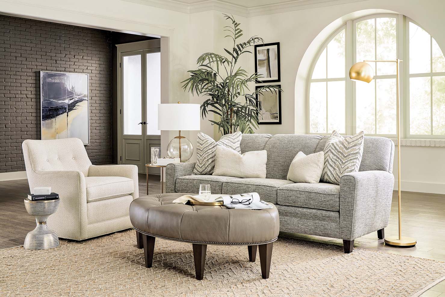 A classic grey couch, white chair, and tufted taupe leather ottoman sit coherently in a living room.