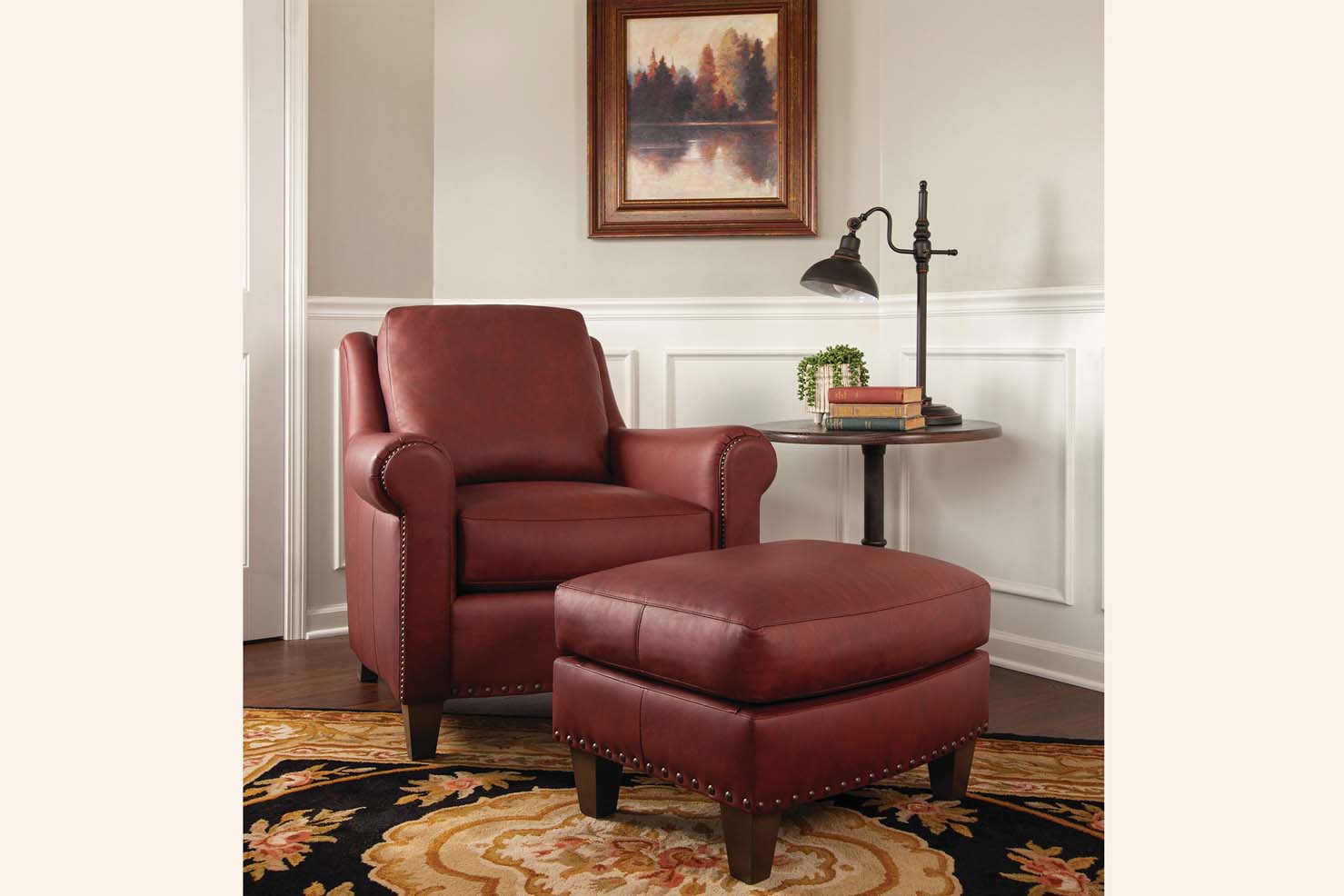 An occasional chair and its matching ottoman is upholstered in a red leather with gold nail heads securing it.