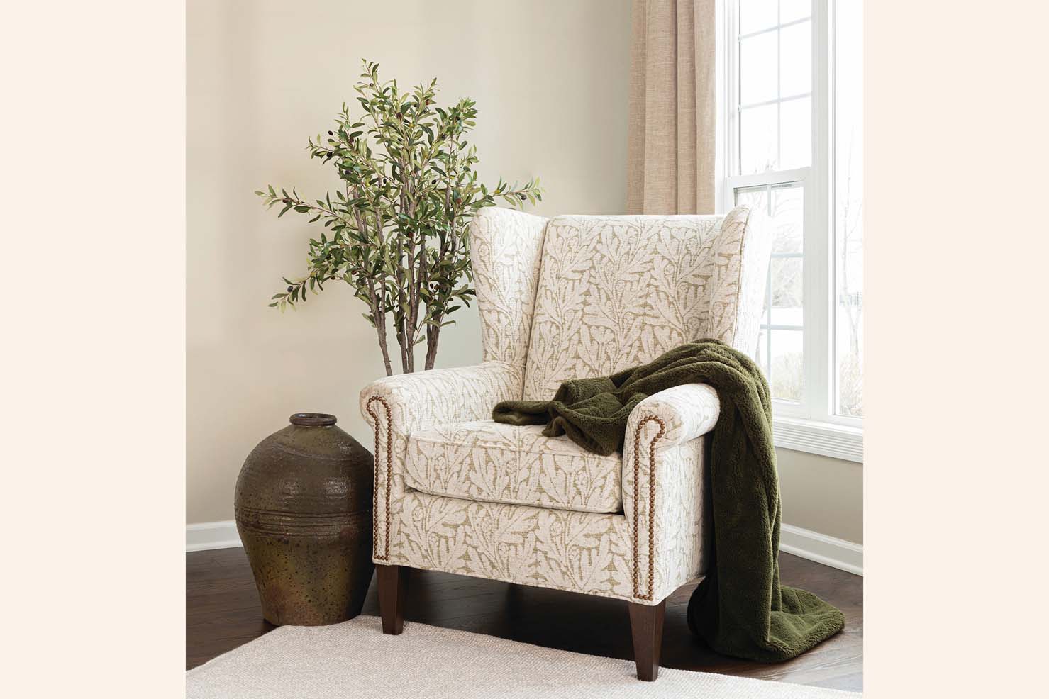 A winged occasional chair is upholstered in a patterned fabric with white leaves on a tan background.