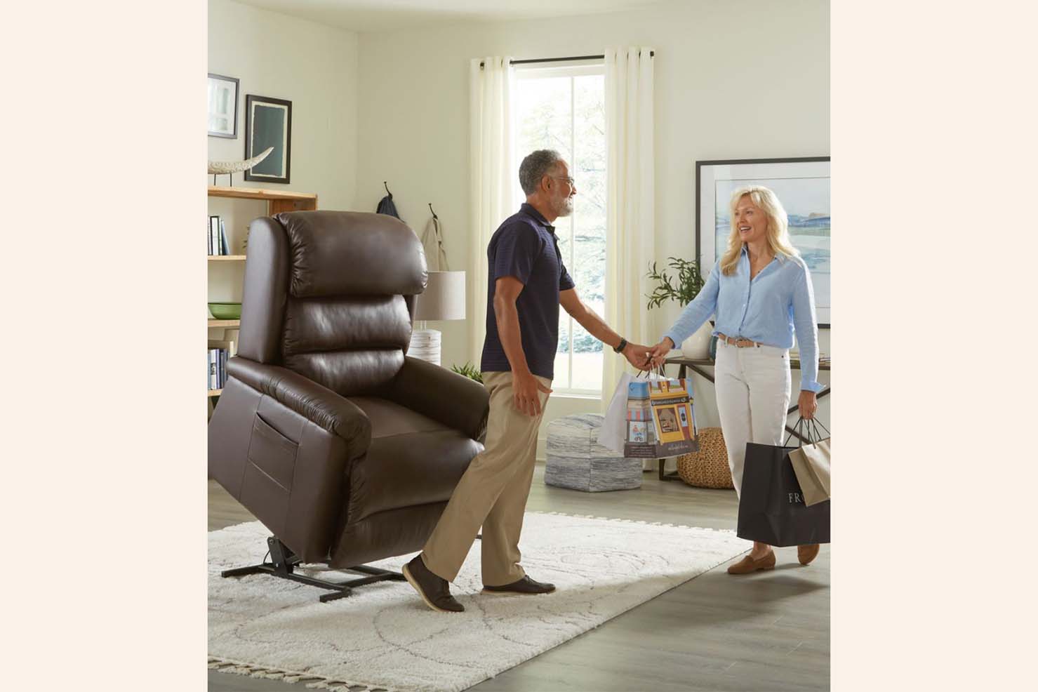 An older man gets up from a dark brown power recliner to greet an older woman
