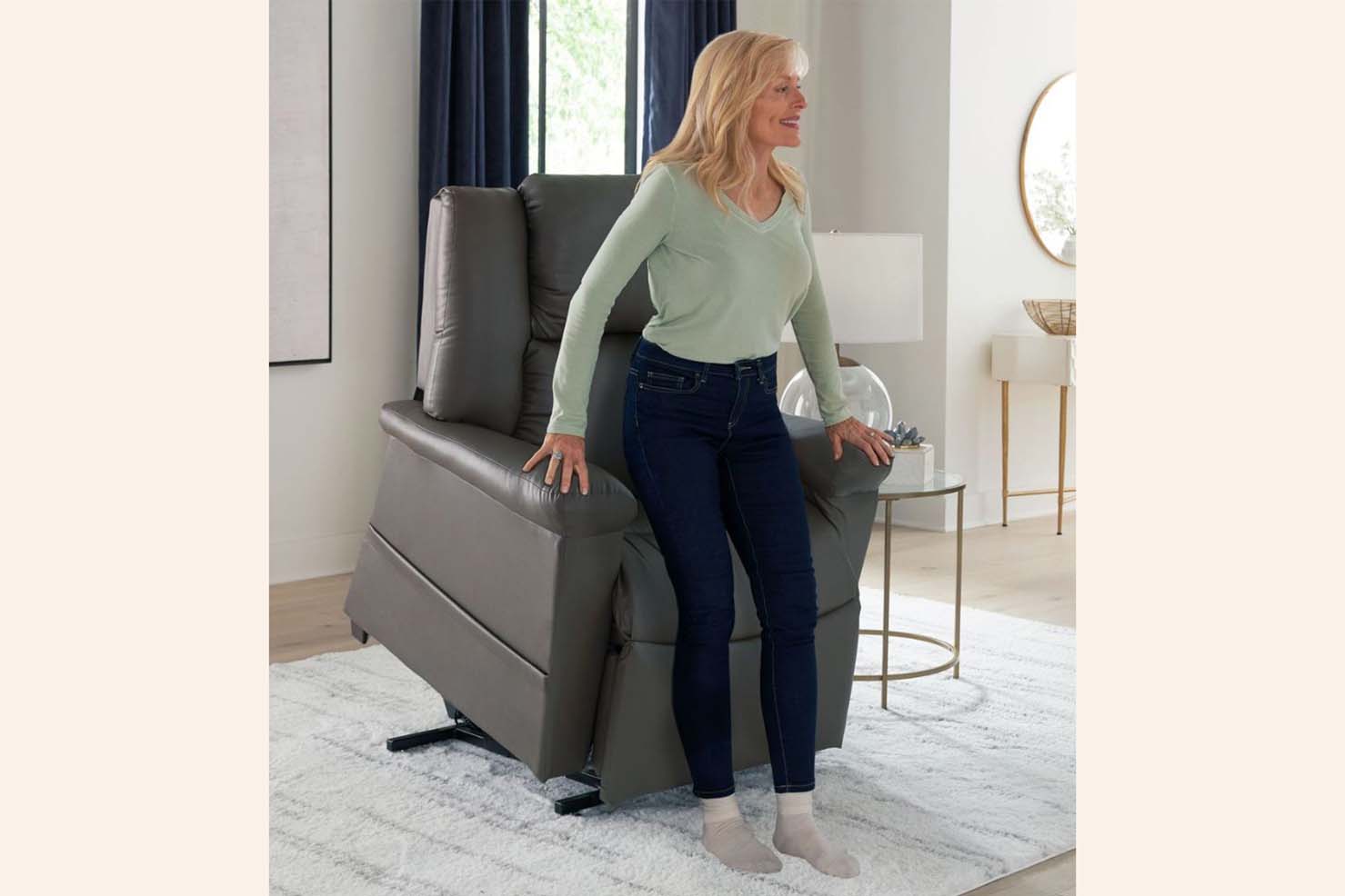 An older woman smiles as she stands up with the aide of the tilted grey power recliner.