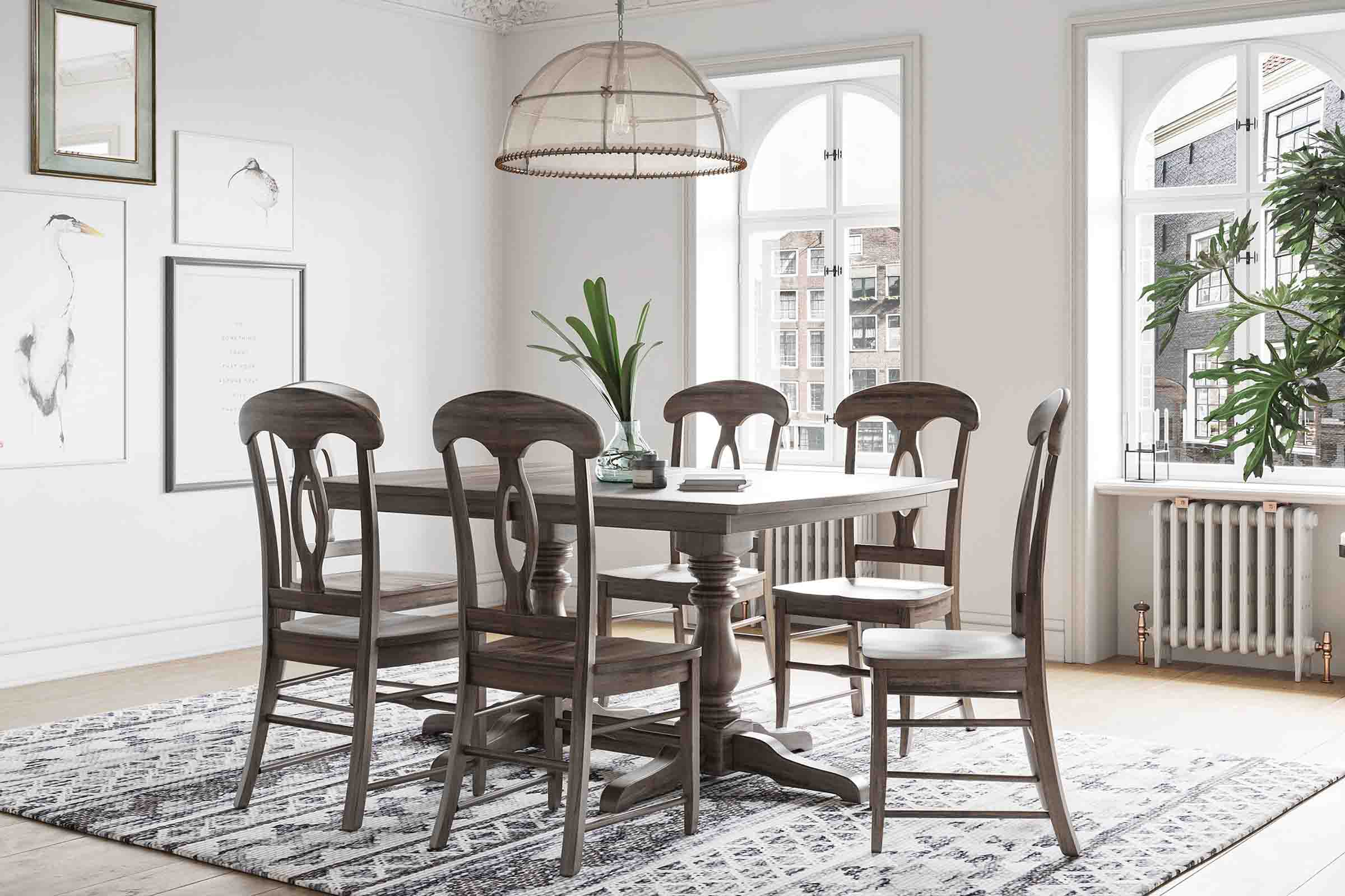 A long dining table with decorative legs sits in a farmhouse style dining room with matching chairs.