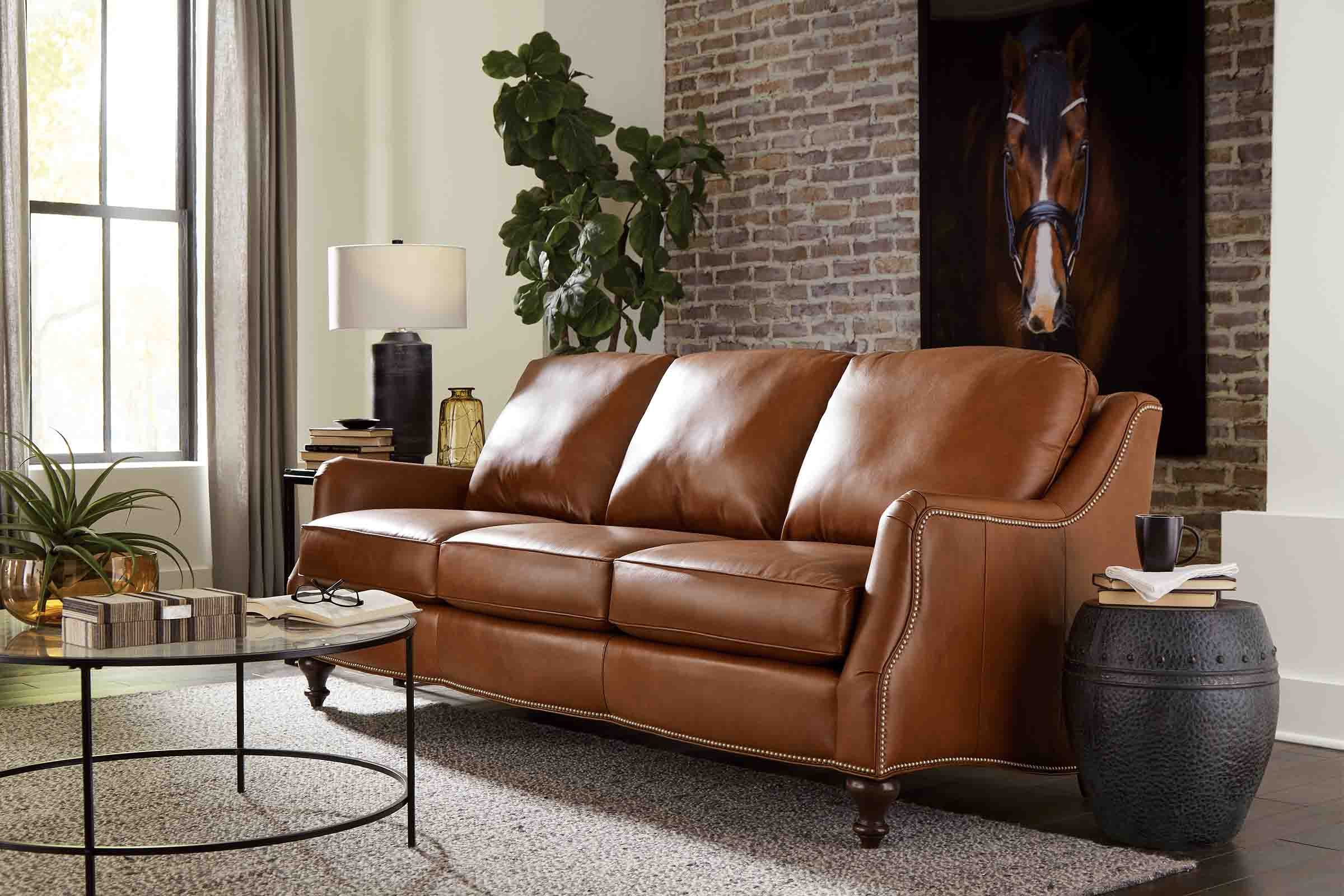 A classic grey couch, white chair, and tufted taupe leather ottoman sit coherently in a living room.