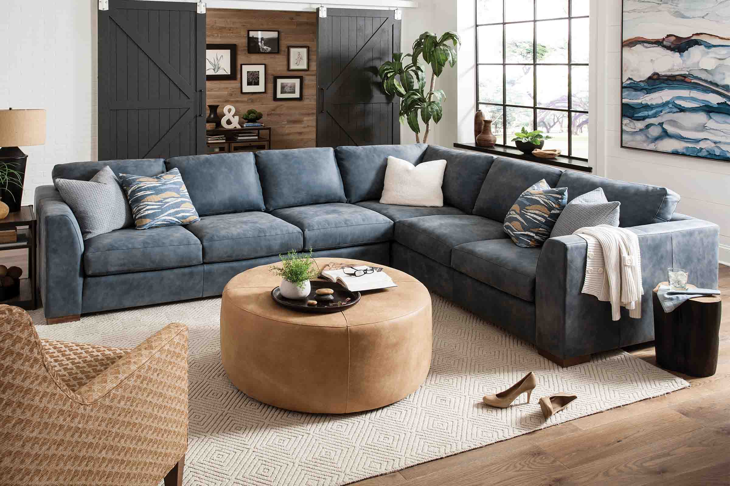 Deep red leather sofa, chair, and ottoman is displayed in a dark grey painted living room. A large patterned rug and glass coffee table accent the furniture.